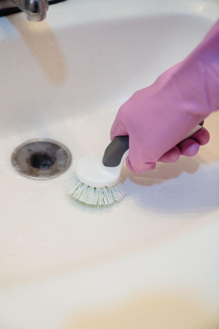project-01-c A close-up shot of a gloved hand scrubbing a sink with a scrub brush.